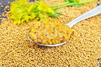 Mustard Dijon sauce in a metal spoon and yellow mustard flower on seeds against a wooden table background