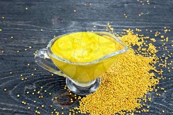 Mustard sauce in a glass sauceboat, mustard seeds against a black wooden board