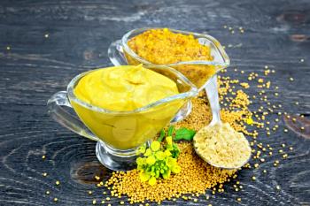 Mustard sauce and Dijon mustard in two glass saucepans, yellow flower, seeds and powder in a spoon on black wooden board background
