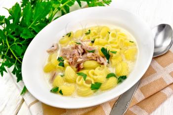 Chicken meat soup, pasta with cream and cilantro in a plate, napkin, parsley, metal spoon on a wooden board background