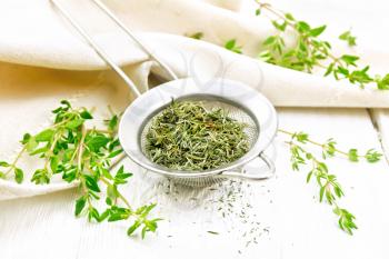 Thyme dry in a metal strainer, fresh greens of grass and linen towel on the background of white wooden board
