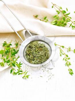 Thyme dry in a metal strainer, fresh greens of grass and linen towel on the background of wooden boards
