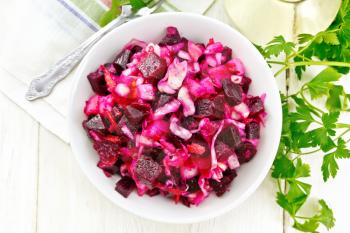 Vinaigrette salad with pickled or sauerkraut, potatoes, beetroot and onions, seasoned with vegetable oil in a bowl, napkin, parsley on a wooden board background from above