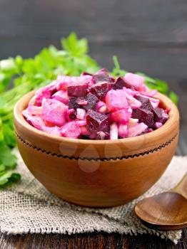 Vinaigrette salad with pickled or sauerkraut, potatoes, beetroot and onions, seasoned with vegetable oil in a bowl on burlap, parsley on a wooden board background