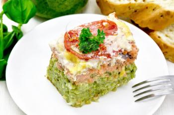 Casserole of salmon and rice with pesto, tomato and cheese in plate, bread, garlic and a jar of sauce on light wooden board background