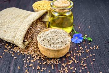 Flax flour in a bowl, seeds in a bag, blue linen flower and oil in a glass jar on a background of a dark wooden board