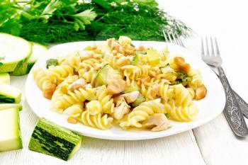 Fusilli pasta with chicken breast, zucchini, cream and pine nuts in a plate, fork and parsley on a wooden board background
