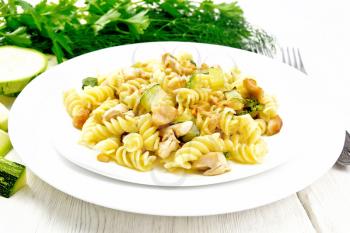 Fusilli pasta with chicken breast, zucchini, cream and pine nuts in two plates, forks and parsley on a white wooden board background
