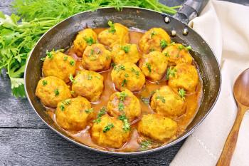 Meatballs with tomato sauce in a frying pan, parsley, dill, napkin and spoon on a wooden board background
