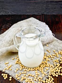 Soy milk in a jug, soybeans on a napkin of burlap on the background of wooden boards