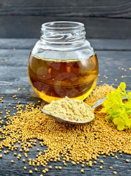 Mustard powder in a spoon, oil in a glass jar, seeds and mustard flower against a black wooden board