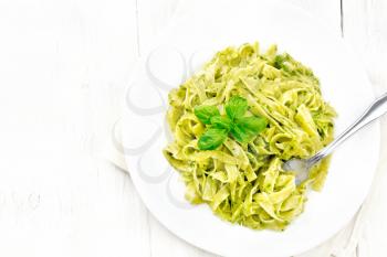Tagliatelle pasta with pesto, basil and fork in a plate on a napkin on wooden board background from above