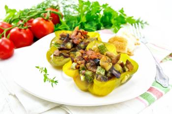 Sweet pepper stuffed with mushrooms, tomatoes, zucchini, eggplant and onions, seasoned with wine, garlic, thyme and spices in white plate on towel against the background of light wooden board