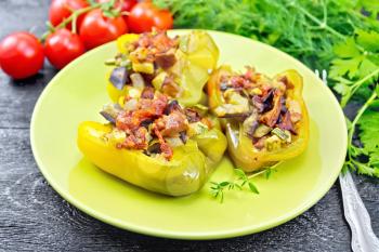 Sweet pepper stuffed with mushrooms, tomatoes, zucchini, eggplant and onions, seasoned with wine, garlic, thyme and spices in a green plate against black wooden board