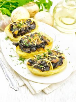 Potatoes stuffed with mushrooms, fried onions and cheese in a plate on napkin, vegetable oil in carafe, parsley, garlic and a fork on wooden board background