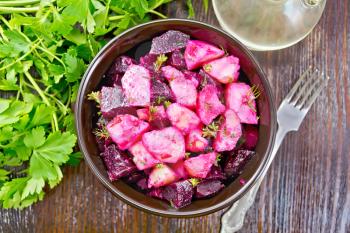 Beetroot and potato salad, seasoned with vegetable oil and vinegar in a bowl, parsley and fork on a wooden board background from above