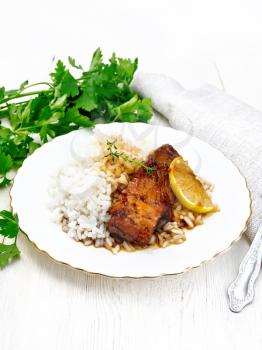 Pink salmon with honey, lemon juice, garlic, hot pepper and soy sauce, boiled rice, a slice of lemon and sprig of thyme in a plate, parsley, towel and fork on the background of light wooden board