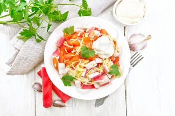 Salad of crab sticks, cheese, garlic and tomatoes with mayonnaise, napkin, parsley on the background of a light wooden board on top