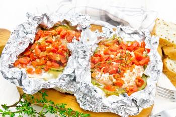 Pink salmon with zucchini, tomatoes, onions, garlic and thyme, baked in foil, fork and bread on the background of a light wooden board