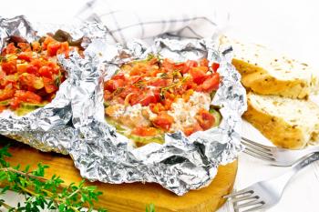 Pink salmon with zucchini, tomatoes, onions, garlic and thyme, baked in foil, fork and bread on a wooden board background