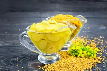Mustard sauce and Dijon mustard in two glass saucepans, yellow flower and seeds against a black wooden board