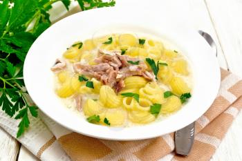 Chicken meat soup, pasta with cream and cilantro in a plate, towel, parsley, metal spoon on a wooden board background