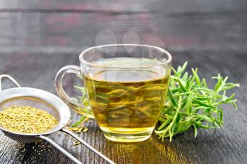 Rosemary herbal tea in a cup, a strainer with dry herb on a dark wooden board background