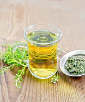Herbal tea in a glass mug of thyme, metal strainer with dry leaves, fresh leaf on a wooden board background