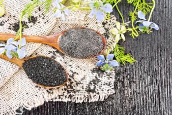 Flour and seeds of Nigella sativa in two spoons on burlap, sprigs of kalingini with blue flowers and green leaves on background of an old wooden board from above
