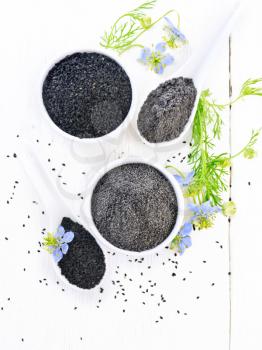 Flour and seeds of black caraway in bowls, sprigs of kalingini with blue flowers and green leaves on a background of light wooden board from above 