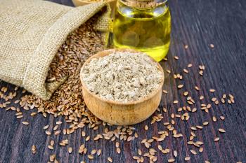 Flax flour in a bowl, seeds in a bag and linseed oil in a glass jar on a wooden board background