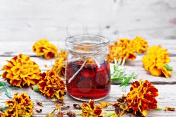 Alcohol tincture of marigolds in a glass jar, fresh and dried flowers with green leaves on wooden board background