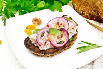 Salad of salmon, petiole celery, raisins, walnuts, red onions and cottage cheese on toasted bread with green lettuce on a plate on a white wooden board background