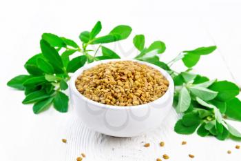 Fenugreek seeds in a bowl and on a table, green seasoning leaves on wooden board background
