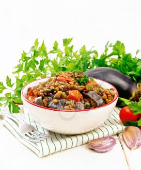 Green lentils stewed with eggplant, tomatoes, garlic and spices in a bowl on a kitchen towel, parsley on light wooden board background
