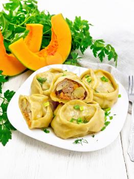 Manty steamed pies with minced meat and pumpkin, green onions in a plate, napkin, parsley and fork on wooden board background