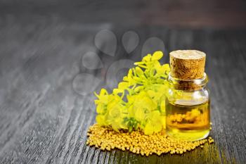 Mustard oil in a glass bottle, grains and yellow flowers on a wooden board background
