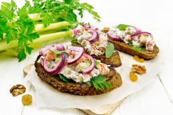 Salmon, petiole celery, raisins, walnuts, red onions and curd cheese salad on toasted bread with green lettuce on paper on a wooden board background
