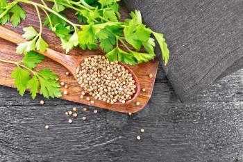 Coriander seeds in a spoon, green fresh cilantro and a napkin on wooden board background from above