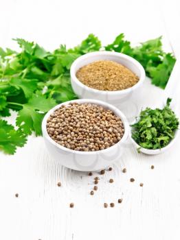 Coriander seeds and ground in two bowls, dried cilantro in a spoon, seasoning greens on wooden board background