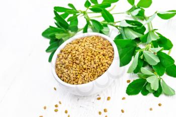 Fenugreek seeds in a bowl and on a table, green seasoning leaves on a light wooden board background