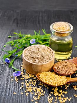 Flaxseed flour in a bowl, white and brown seeds in two spoons and on table, leaves and blue flax flowers, oil in a glass jar on black wooden board background
