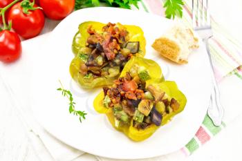 Sweet pepper stuffed with mushrooms, tomatoes, zucchini, eggplant and onions, seasoned with wine, garlic, thyme and spices in white plate on a towel against the background of wooden boards