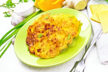 Fritters of pumpkin, cheese and ginger in a green plate, sour cream in a bowl, napkin, parsley and fork on wooden board background
