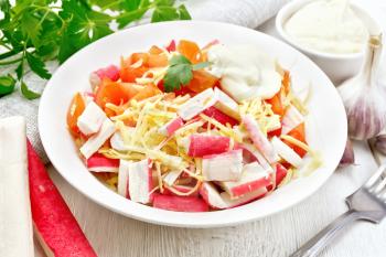 Salad of crab sticks, cheese, garlic and tomatoes with mayonnaise, napkin, parsley on the background of a light wooden board