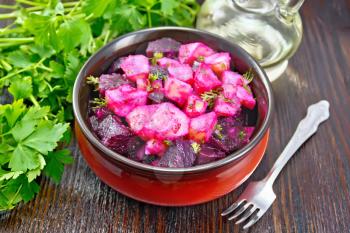Salad of beets and potatoes, seasoned with vegetable oil and vinegar in a bowl, parsley and a fork on a wooden board background
