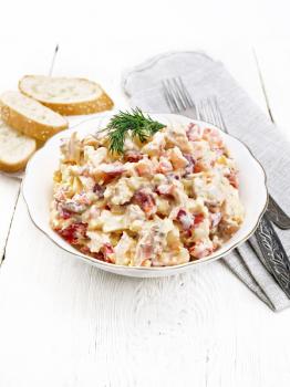 Salad with chicken, sweet pepper, tomato, egg and cheese seasoned with mayonnaise and garlic in a dish, napkin, bread and forks on a light wooden board background