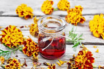 Alcohol tincture of marigolds in a glass jar, fresh and dried flowers on background of an old wooden board