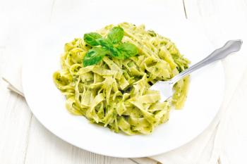 Tagliatelle pasta with pesto, basil and fork in a plate on a towel against the background of light wooden boards
