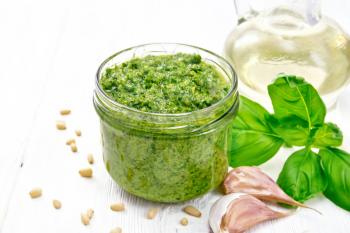 Pesto sauce in a glass jar, basil, pine nuts, garlic and olive oil on light wooden board background
